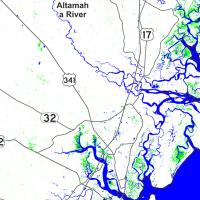 The rectangular image is a map of the St. Simons Island area of coastal Georgia. Land is colored white, roadways are black, inundated vegetation area are green, and water is colored blue. The Atlantic Ocean is in the lower-right of the image and its blue shaded area extends into waterways along the coast.