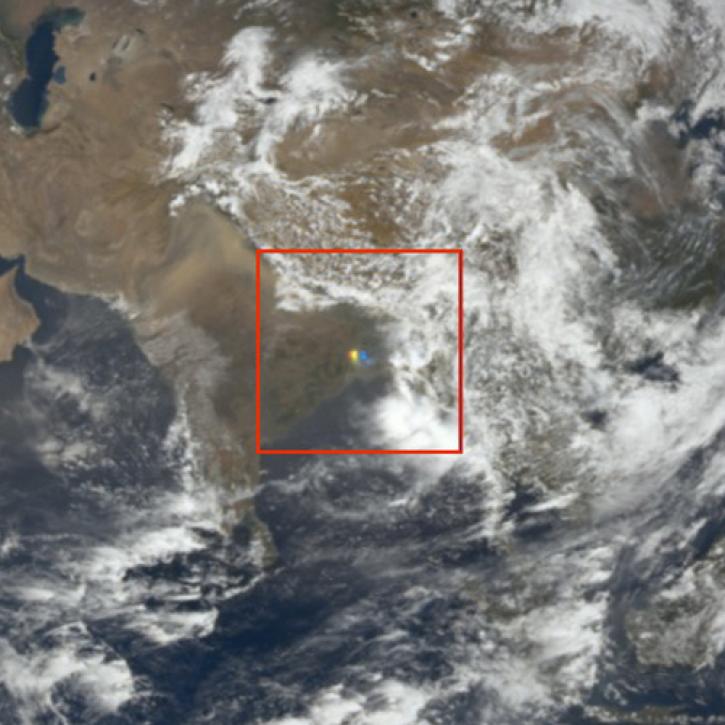 This is a rectangular image of a sunglint over land. The upper two-thirds of the image shows land with clouds floating over it. The lower third of the image is largely ocean. In the center of the image is a red outline of a square and in the center of the square is a red, green, and blue sunglint.