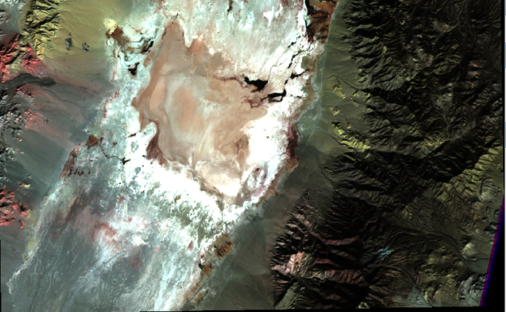 False‑color composite (ASTER bands 4, 6, and 8) of Railroad Valley, Nevada, showing a bright, irregular salt‑flat basin surrounded by dark, rugged mountain terrain.