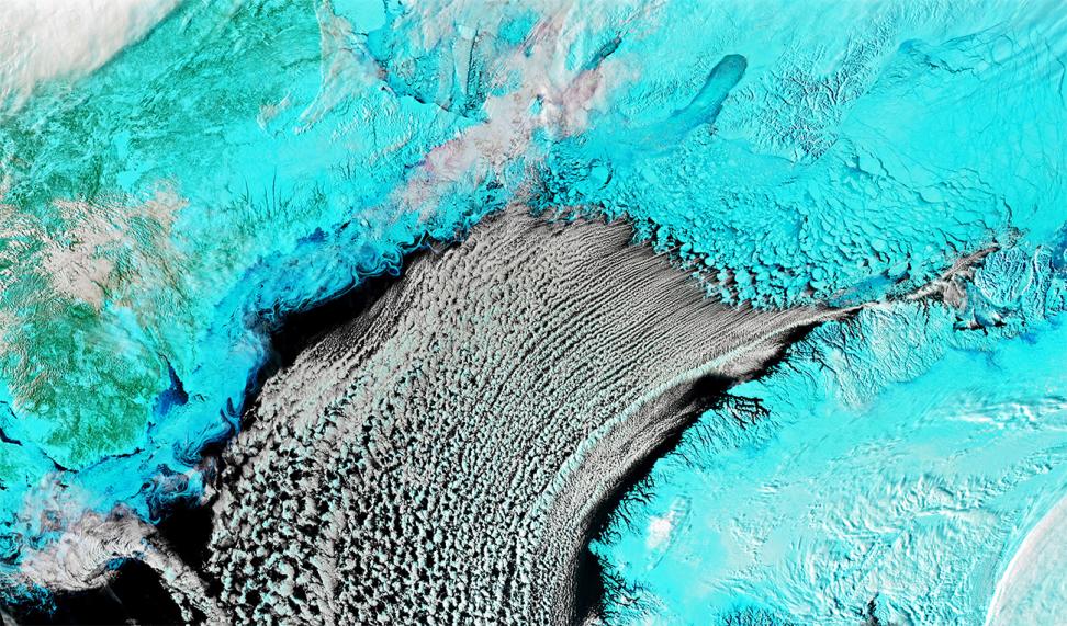 False color image with land and ice appearing as teal and clouds in white.