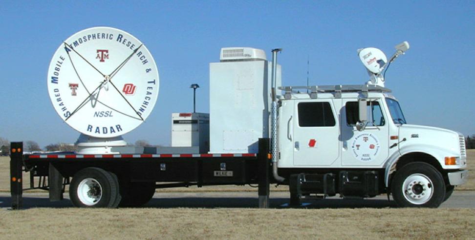 Outside image of large truck flatbed carrying large white instrument with a large white antenna.