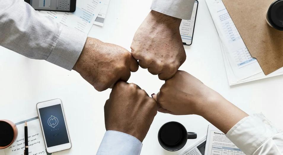 Close up of four fists, each showing a white work shirt to the wrist, tapping as if to celebrate being a team