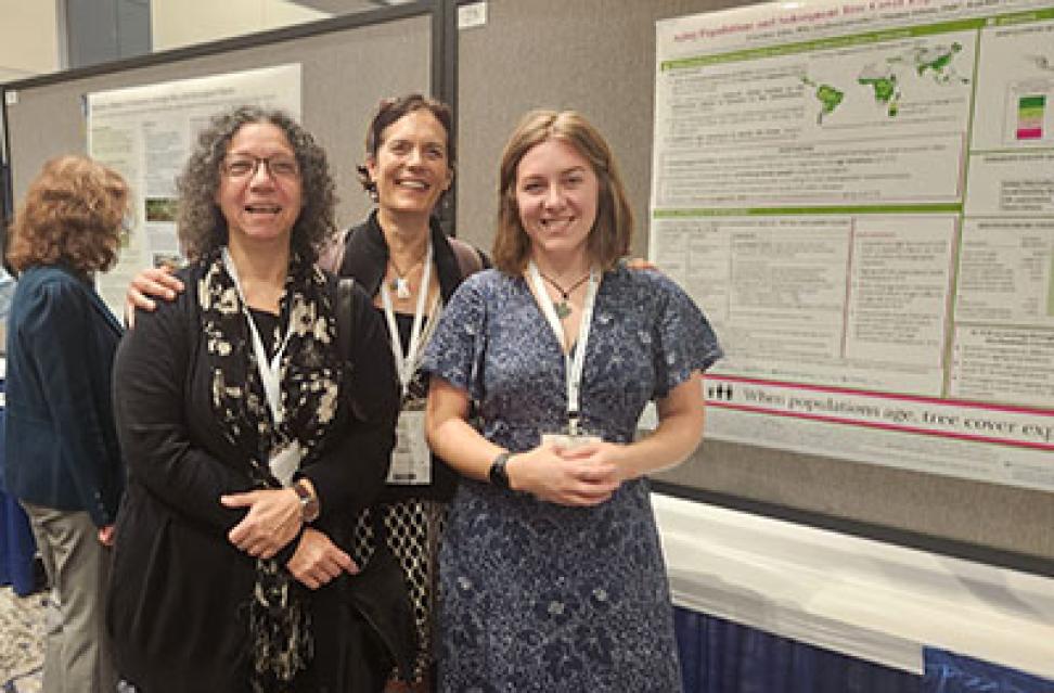 Three women at a conference stand in front of a poster.