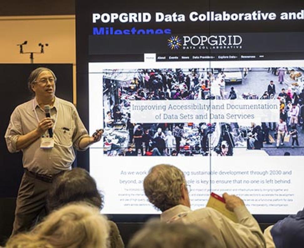 Robert Chen stands in front of NASA's Hyperwall screen, which displays information about population data.