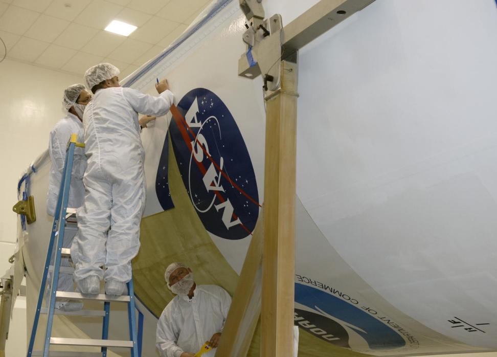 Technicians apply the NASA logo decal next to the NOAA logo decal to the fairing that will encapsulate the GOES-O satellite during launch.