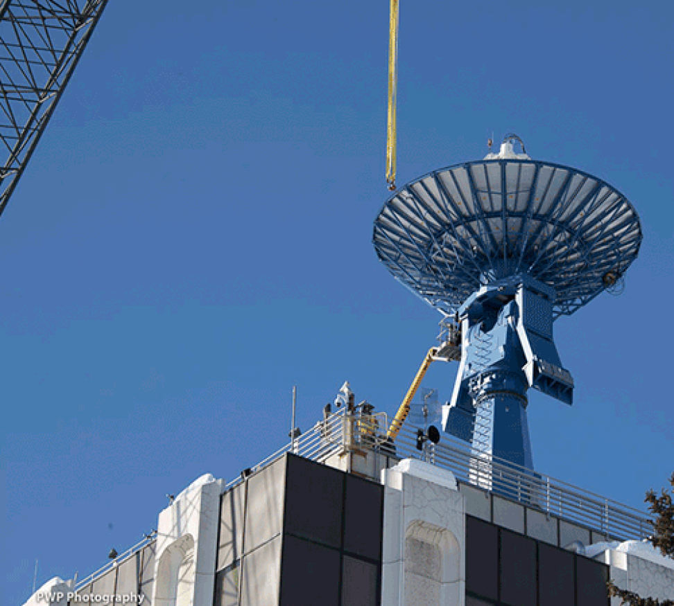 A 250-foot crane lifts the original antenna off the top of the Elvey Building, framed by an outdoor rocket display, part of the Geophysical Institute.