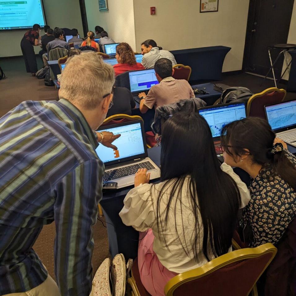 Three people huddle around an open laptop, with one person pointing at the screen.