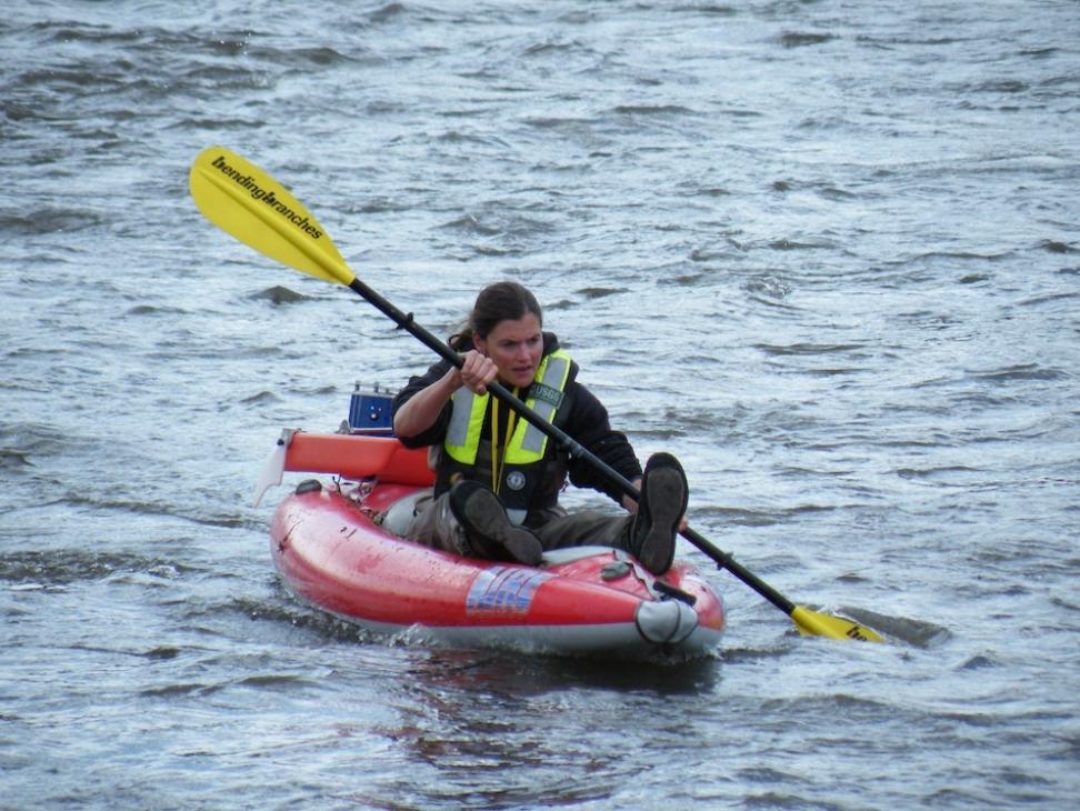 A person in a red kayak navigates a body of water with a yellow paddle.