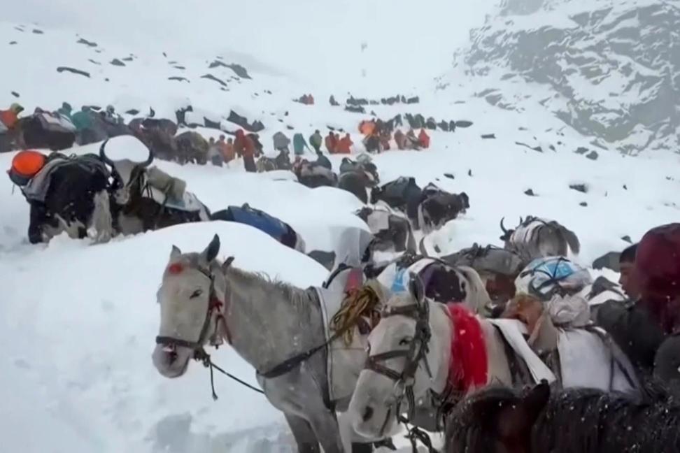 Horseback riders trek through snowy mountain terrain.