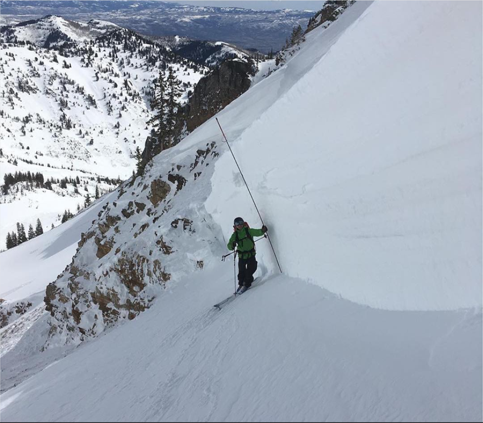 Man measuring side of snow bank in the mountains.