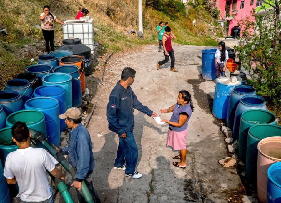 Photograph of people waiting near rows of barrels that will be filled with water