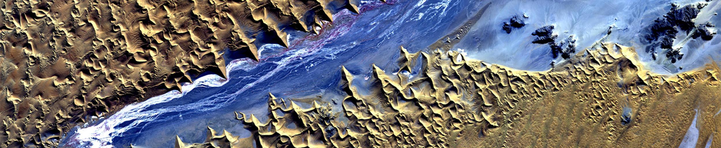 This ALOS AVNIR-2 image shows a part of the southern Namib desert called the Sossusvlei, or “dead-end marsh” – a salt-clay pan surrounded by dunes sometimes reaching almost 400 meters high. The Tsauchab River flows between the dunes, and in most years, the river runs dry before reaching the vlei, or marsh. Because of the visible and near-infrared imaging capability of the satellite sensor, the contrast between the sand dunes and salt and clay of the river basin is obvious. Vegetation growing along the river
