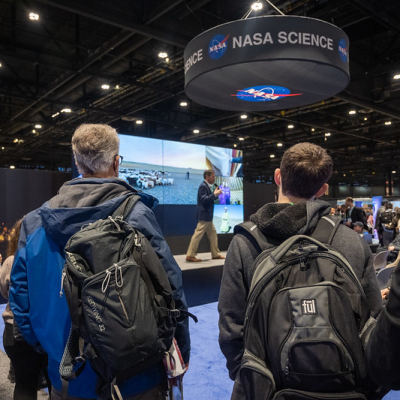 Person standing in front of the NASA hyperwall with a NASA Science banner over head.