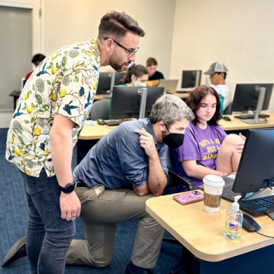 Two professors standing over a student working at a computer