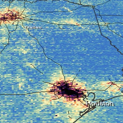 This a square image of a portion of Eastern Texas. The image was taken by the TEMPO spacecraft and shows nitrogen dioxide gas levels across the region. A majority of the image is colored blue indicating lower levels of gas. The upper left corner of the image shows the city of Dallas colored in orange, red, and black indicating increasingly higher levels of gas. In the lower middle of the image is Houston, again colored in orange, red, and black indicating increasingly higher levels of gas.