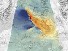 This is a primarily grayscale, topographic image showing the ridges, peaks, valleys, and flatlands of the area.In the center of the image is a swath of area highlighted in green. Within that zone are areas on the left side colored blue, and areas colored orange and red on the right.