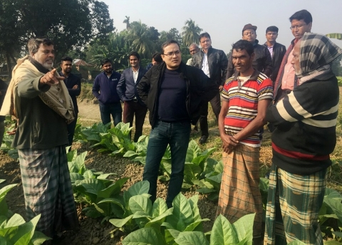 Image of Dr. Hossain standing in a planted field and wearing black talking with several farmers wearing native dress.